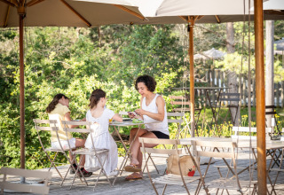 Famiglia che fa colazione all'aperto sotto ombrelloni presso il glamping Village Huttopia Lanmary-Périgord.