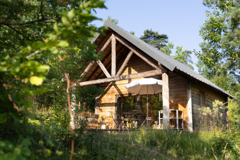 Wooden cabin surrounded by greenery at Village Huttopia Lanmary-Périgord – Glamping Dordogne, perfect for nature escapes.