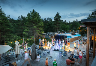 Village Huttopia Lanmary-Périgord : scène de glamping avec invités, estrade, guirlandes et forêt en arrière-plan.