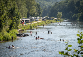 Camping au bord de la rivière à Huttopia Vallée de la Semois, Ardenne, avec nageurs et campeurs détendus.