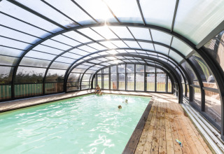 Piscina cubierta con estructura de vidrio y tarima de madera en Huttopia Vallée de la Semois, Ardenas, glamping.
