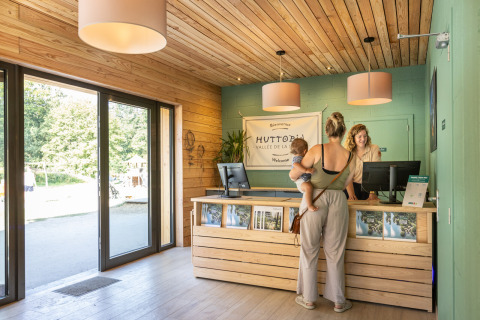 Reception area of Huttopia Vallée de la Semois glamping in Ardennes, guest with child at check-in desk.