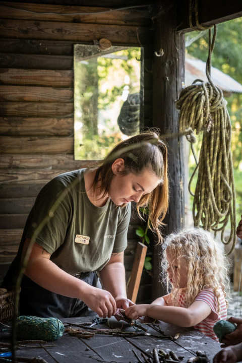 Eine Frau bastelt gemeinsam mit einem Kind in einer gemütlichen Holzhütte bei Huttopia Vallée de la Semois.