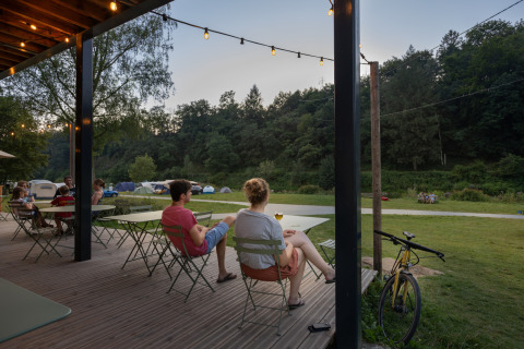 Des personnes se détendent en terrasse au glamping Huttopia Vallée de la Semois, au cœur des Ardennes.