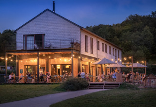 Evening at Huttopia Vallée de la Semois glamping in the Ardennes with guests dining on a cozy outdoor terrace.