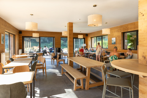 Indoor communal area at Huttopia Vallée de la Semois glamping in the Ardennes with guests at tables.