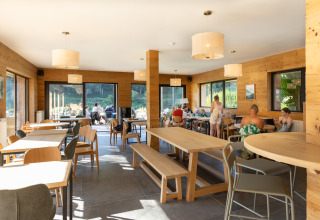 Area comune interna del glamping Huttopia Vallée de la Semois nelle Ardenne con ospiti ai tavoli.