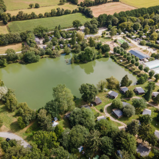 Vista aerea di Huttopia Baie du Mont Saint Michel glamping con lago, chalet e natura verde intorno.