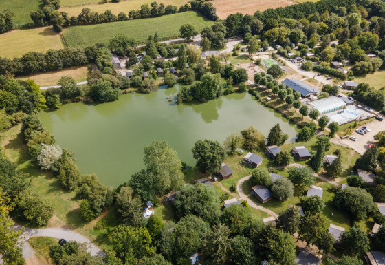 Vue aérienne du site glamping Huttopia Baie du Mont Saint Michel avec lac, cabanes et espaces verts.