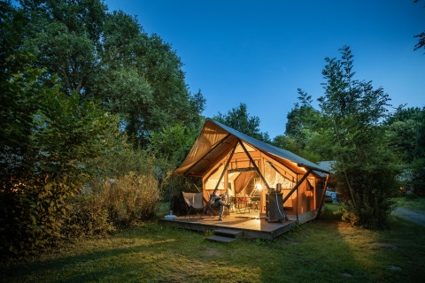 Verlicht glampingverblijf in de avond bij Huttopia Baie du Mont Saint Michel, omgeven door groene natuur.