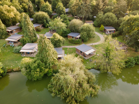 Luftaufnahme von Glamping-Unterkünften am See bei Huttopia Baie du Mont Saint Michel, umgeben von Bäumen.