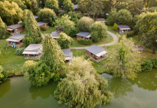 Luchtfoto van glampingaccommodaties aan het meer bij Huttopia Baie du Mont Saint Michel, omgeven door bomen.