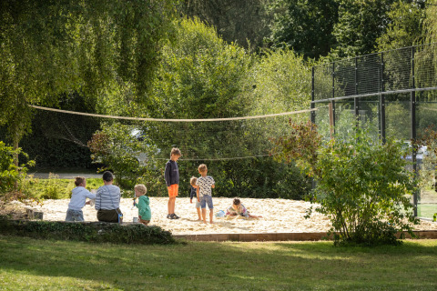 Children and adults play in a sandpit below a volleyball net at Huttopia Baie du Mont Saint Michel – Glamping Bretagne.