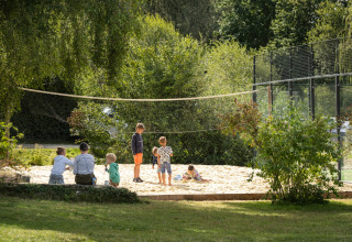 Kinderen en volwassenen spelen in een zandbak onder een volleybalnet bij Huttopia Baie du Mont Saint Michel – Glamping Bretagne.