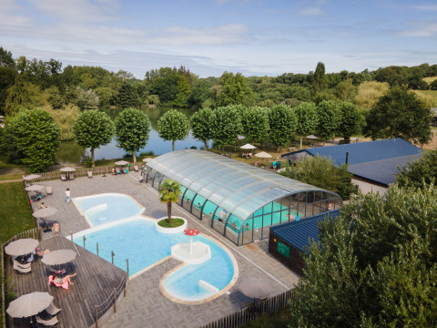 Piscine extérieure et piscine couverte près d’un lac entouré d’arbres à Huttopia Baie du Mont Saint Michel.
