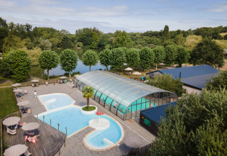 Udendørs pool og overdækket swimmingpool ved sø omgivet af grønne træer på Huttopia Baie du Mont Saint Michel.