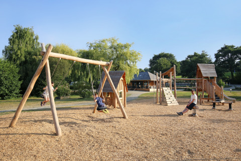 Niños juegan en columpios de madera y estructuras de juego en Huttopia Baie du Mont Saint Michel Glamping Bretagne.