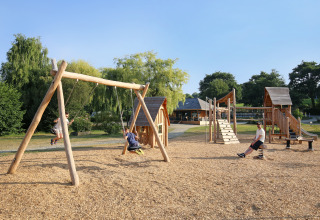 Des enfants jouent sur des balançoires et jeux en bois à Huttopia Baie du Mont Saint Michel Glamping Bretagne.