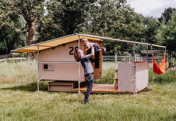 Buiten glamping accommodatie waar een man een kind optilt voor een zomer chalet op het gras.