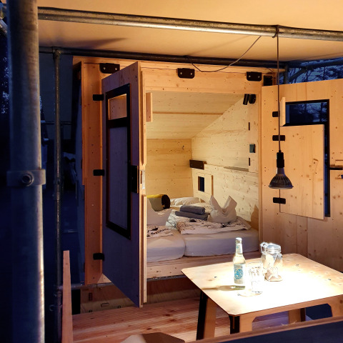 Glamping-Unterkunft aus Holz mit Bett, Tisch und Lampe im Chalet Destinature Südeifel, Sommerchalets Eifel.