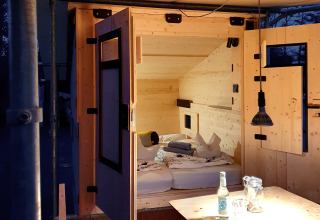 Cozy glamping cabin interior with wooden bed, table, and soft lighting at Chalet Destinature Südeifel, Eifel.