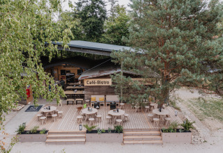 Terras van het Café-Bistro bij Chalet Destinature Südeifel glamping, omringd door bomen in zomerse sfeer.