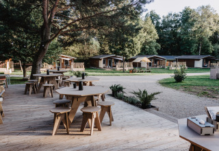Terraza exterior con mesas y sillas frente a cabañas glamping en Chalet Destinature Südeifel en la región Eifel.