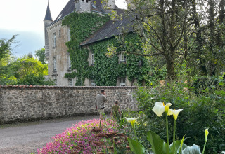 Twee personen wandelen langs een stenen muur voor een met klimop begroeid kasteel bij Vieflow Lodge Dordogne.
