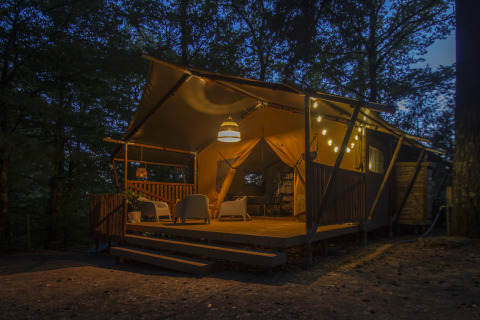 Tienda de glamping iluminada en Vieflow Lodge - Lodgetenten Dordogne, situada en el bosque al anochecer.