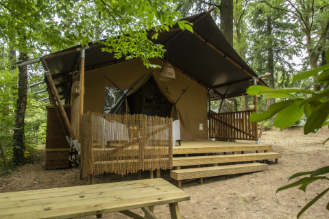 Glamping-Unterkunft Vieflow Lodge in der Dordogne mit Safarizelt und Holzterrasse im grünen Wald.