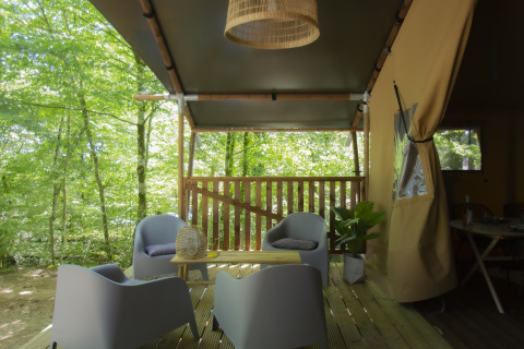 Überdachte Terrasse der Vieflow Lodge - Lodgetenten Dordorgne mit modernen Stühlen und Waldblick.