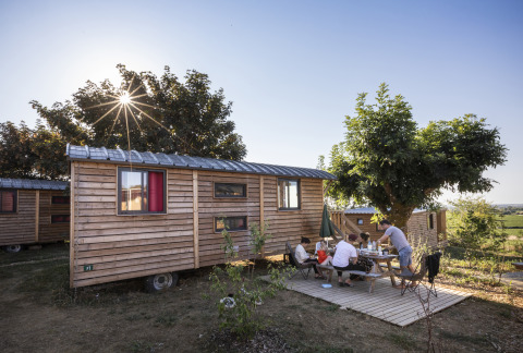 Familie nyder udendørs måltid ved træhytte under solskin på Huttopia Meursault - Glamping Bourgogne.