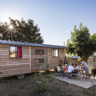 Family having an outdoor meal by a wooden cabin at Huttopia Meursault - Glamping Bourgogne on a sunny day.