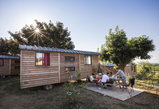 Familie nyder udendørs måltid ved træhytte under solskin på Huttopia Meursault - Glamping Bourgogne.