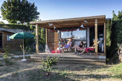 Glampingverblijf Huttopia Meursault - Glamping Bourgogne, mensen genieten ontspannen op de veranda in de zon.