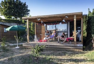 Glamping-indkvartering Huttopia Meursault i Bourgogne med mennesker, der nyder verandaen på en solrig dag.