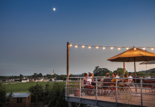 Outdoor terrace at Huttopia Meursault - Glamping Bourgogne, people dining at dusk overlooking rural scenery.