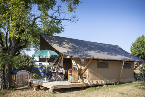 Familie entspannt vor einem Safarizelt auf Huttopia Meursault - Glamping Bourgogne an einem sonnigen Morgen.