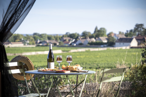 Mesa al aire libre con vino, copas, pan y queso en un glamping sobre viñedos en Huttopia Meursault, Borgoña.