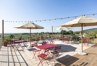 Buitenterras bij Huttopia Meursault - Glamping Bourgogne met rode tafels, parasols en uitzicht over het landschap.