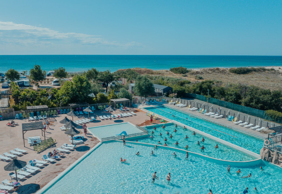Grande zone de piscine extérieure avec glamping, transats et vue sur la mer au Camping Beach Garden Sud de la France.