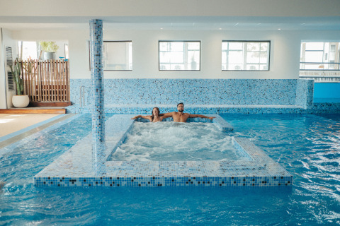 Zona de piscina cubierta con dos personas relajándose en un jacuzzi en Camping Beach Garden - Glamping Sur de Francia.