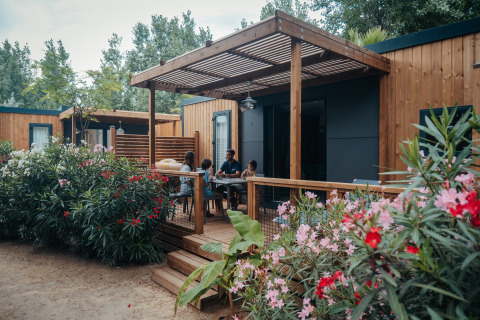 Familie entspannt auf Holzterrasse vom Glamping Camping Beach Garden in Südfrankreich, umgeben von Blumen.