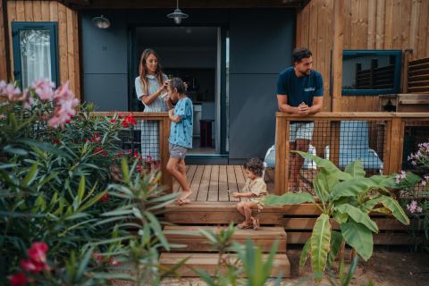 Een gezin geniet op de veranda van hun glampingaccommodatie, omgeven door bloemen en groene planten.