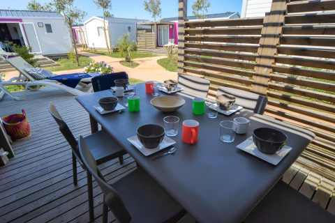 Table dressée en terrasse boisée, hébergements glamping en arrière-plan au Camping Beach Garden, Sud de la France.