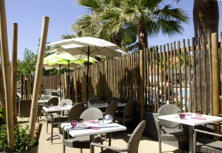 Espace repas extérieur avec parasols et chaises en osier au Camping Beach Garden - Glamping Sud de la France.