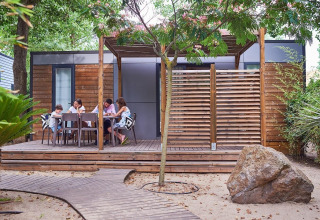 Family dining on the deck of a modern wooden glamping cabin at Camping Beach Garden in South France.