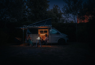 Deux personnes profitent d’un van éclairé sous des guirlandes la nuit, glamping Camping Beach Garden.