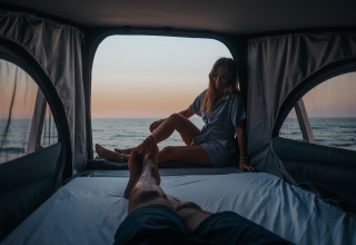 Twee mensen genieten van de zonsondergang boven zee in een glamping-accommodatie bij Camping Beach Garden.