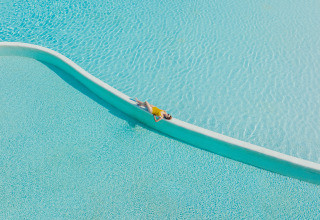 Person relaxing on the edge of a clear blue pool at Camping Beach Garden - Glamping South France.